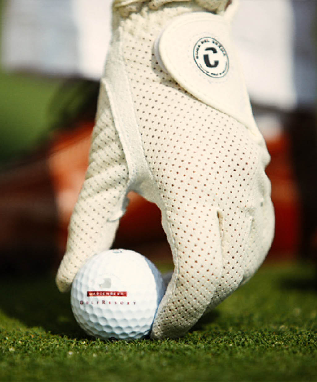 Ein Golfer mit einem perforierten weißen Handschuh platziert einen Golfball auf dem Grün, der das Logo eines Golfresorts trägt. Diese Aufnahme betont die hochwertigen Golfanlagen und den exklusiven Service eines luxuriösen Golfhotels.