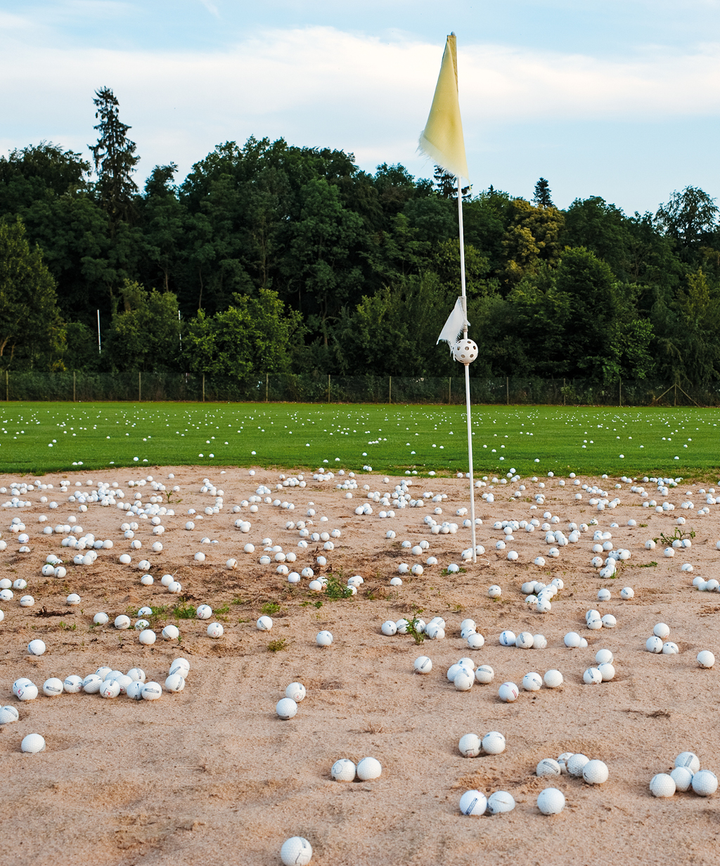 Ein Übungsbunker auf einem Golfplatz, übersät mit Golfbällen, neben einer Fahne. Die Übungsanlage bietet Golfern die Möglichkeit, ihre Technik zu verfeinern, und ist Teil der hochwertigen Einrichtungen, die ein exklusives Golfhotel bietet.