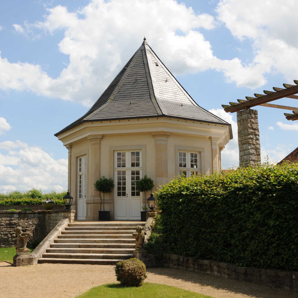 Romantischer Pavillon mit einem eleganten, achteckigen Dach und steinernen Treppen, umgeben von gepflegtem Grün. Dieser Pavillon bietet eine idyllische Kulisse für Hochzeitszeremonien oder Fotoshootings im Freien.